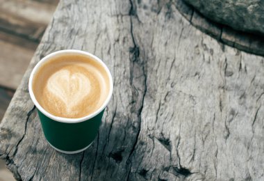 Ahşap zemin üzerinde kalp şeklinde köpük olan bir fincan kahve.. 