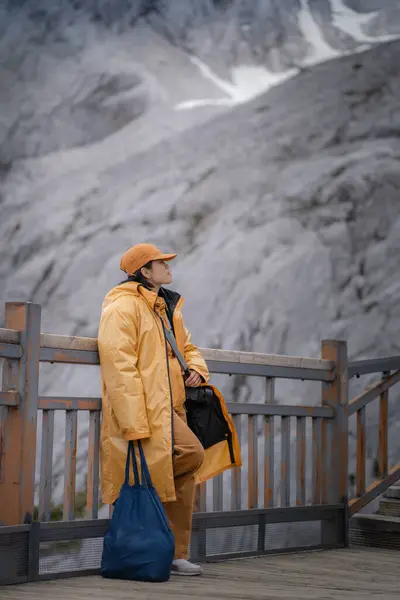 Dağların arka planında şapkalı genç bir kadın ve uzaktan bir sırt çantası.