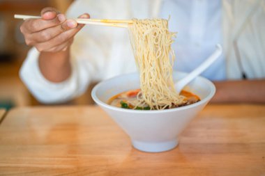 Meçhul bir kadın yemek çubuklarıyla erişteli lezzetli ramen çorbası yiyor ve Ramen restoranında beyaz kasede et yiyor..