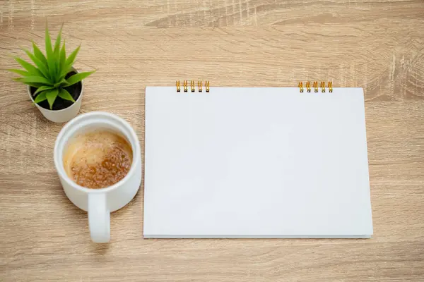 Saksı çiçeği, boş not defteri ve bir fincan kahve.