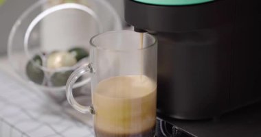 Evdeki mutfakta şeffaf bardakta kapuçino hazırlayan kapsüllü kahve makinesini kapat. Espresso kafein üreticisi ve kremalı İtalyan içeceği.