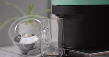 Evdeki mutfakta şeffaf bardakta kapuçino hazırlayan kapsüllü kahve makinesini kapat. Espresso kafein üreticisi ve kremalı İtalyan içeceği.