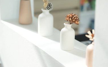 Beyaz seramik vazolar, kurumuş dallar ve modern iç mekanlarda dekoratif elementler.