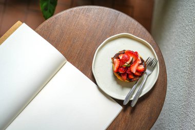 Çilekli kek ve boş defter sehpanın üstünde. 