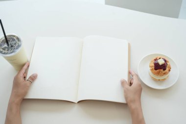 Kadın kafede boş bir defter, masada içki ve pasta açıyor.