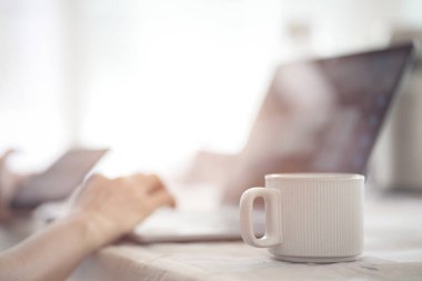 Bilgisayarda çalışan, elinde kahve fincanı tutan ve klavyede yazan kadın eli.