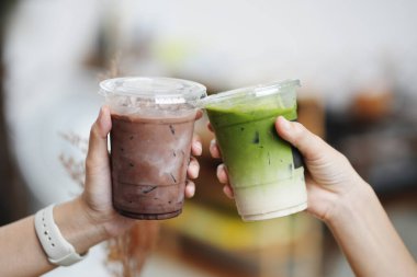 Kafede bir bardak buzlu çikolata ve kibrit yeşil çay tutan genç kızların elleri..