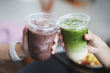 Kafede bir bardak buzlu çikolata ve kibrit yeşil çay tutan genç kızların elleri..