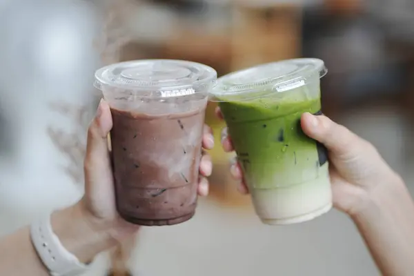 Kafede bir bardak buzlu çikolata ve kibrit yeşil çay tutan genç kızların elleri..