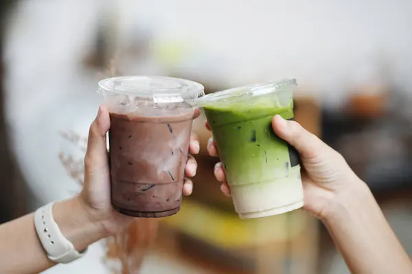 Kafede bir bardak buzlu çikolata ve kibrit yeşil çay tutan genç kızların elleri..
