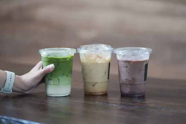 Kafe 'deki ahşap masada elinde buzlu kibrit latte ve bir bardak buzlu kahve ve çikolata tutan bir kadın..