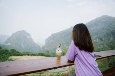 Dağların arkasında bir fincan kahvesi olan genç bir kız. 