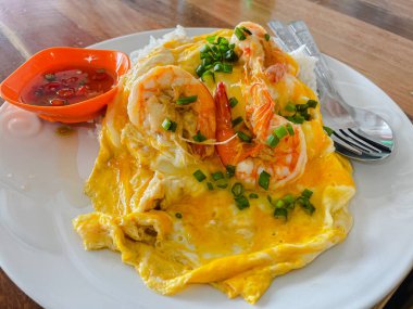 Top view of steamed rice topped with creamy egg sauce and large cooked shrimp on white plate on wooden table.