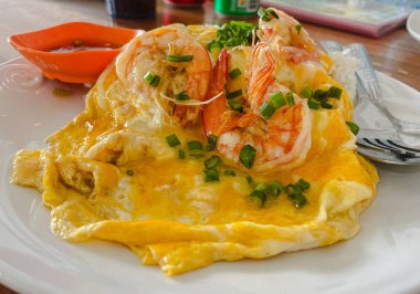 Top view of steamed rice topped with creamy egg sauce and large cooked shrimp on white plate on wooden table.