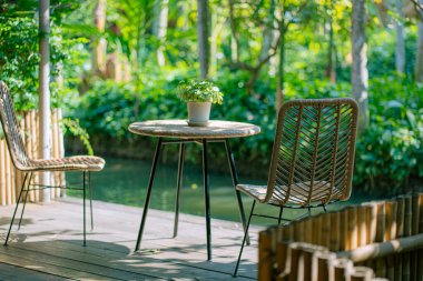 Kaliteli ahşap bir masa, kahverengi sandalyeler ve arka planda iç mekan bitkileri olan klasik bir kafe. Hoş geldin atmosferi yaratıyor.