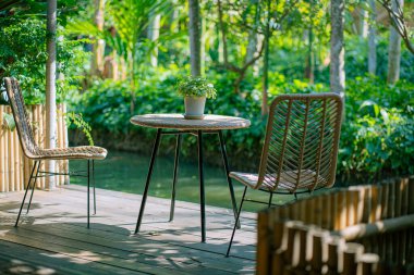 Kaliteli ahşap bir masa, kahverengi sandalyeler ve arka planda iç mekan bitkileri olan klasik bir kafe. Hoş geldin atmosferi yaratıyor.