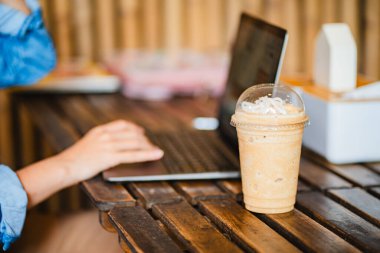 Ofisteki masada dizüstü bilgisayarlı buzlu kahve bardağını kapat. Çalışma alanı kavramı..