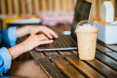 Ofisteki masada dizüstü bilgisayarlı buzlu kahve bardağını kapat. Çalışma alanı kavramı..