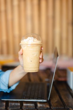 Ofisteki masada dizüstü bilgisayarlı buzlu kahve frappe bardağını kapat. Çalışma alanı kavramı..
