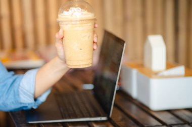 Ofisteki masada dizüstü bilgisayarlı buzlu kahve frappe bardağını kapat. Çalışma alanı kavramı..