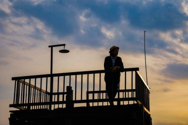 Şapkalı kadın gün batımında iskelede duruyor. 