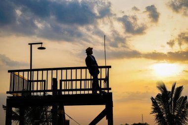 Şapkalı kadın gün batımında iskelede duruyor. 