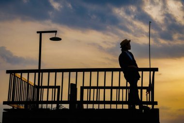 Şapkalı kadın gün batımında iskelede duruyor. 