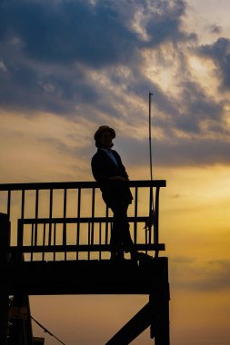 Şapkalı kadın gün batımında iskelede duruyor. 