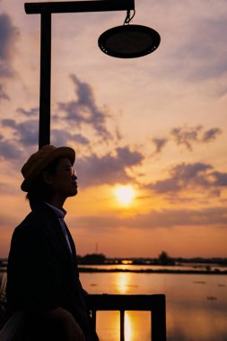 Genç Asyalı kadın gün batımında iskelede vakit geçiriyor. 