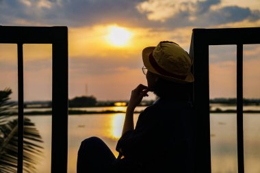 Gün batımına bakan bir kadının silueti.