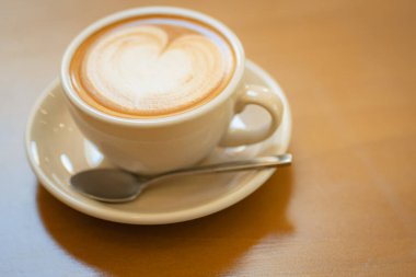 Sütlü kahvenin üstünde beyaz bir fincanda, ahşap masada.