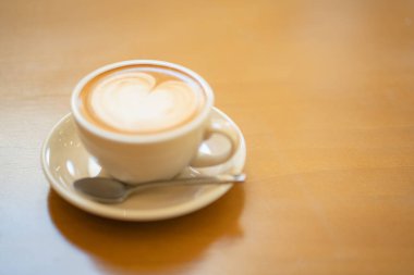 Sütlü kahvenin üstünde beyaz bir fincanda, ahşap masada.