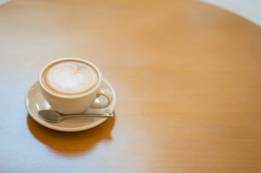 Sütlü kahvenin üstünde beyaz bir fincanda, ahşap masada.