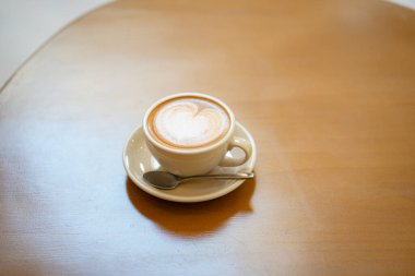 Sütlü kahvenin üstünde beyaz bir fincanda, ahşap masada.