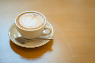 Sütlü kahvenin üstünde beyaz bir fincanda, ahşap masada.