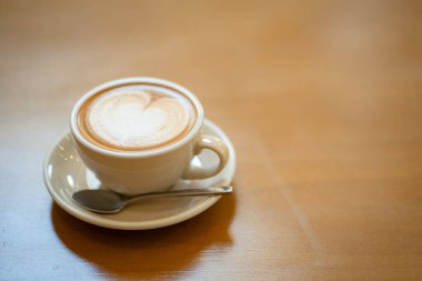 Sütlü kahvenin üstünde beyaz bir fincanda, ahşap masada.
