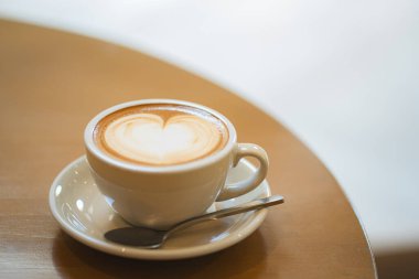 Sütlü kahvenin üstünde beyaz bir fincanda, ahşap masada.