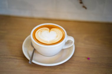 Sütlü kahvenin üstünde beyaz bir fincanda, ahşap masada.