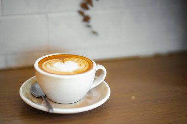 Sütlü kahvenin üstünde beyaz bir fincanda, ahşap masada.