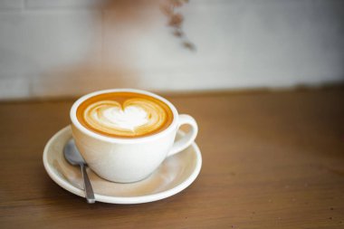 Sütlü kahvenin üstünde beyaz bir fincanda, ahşap masada.