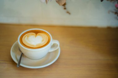 Sütlü kahvenin üstünde beyaz bir fincanda, ahşap masada.