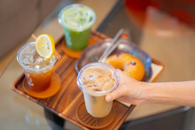 Kahve masasında elinde buzlu latte tutan biri. Yanında da espresso tonik ve buzlu kibrit gibi içkiler.