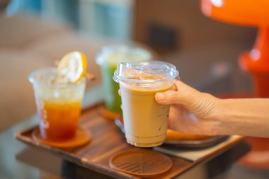 Kahve masasında elinde buzlu latte tutan biri. Yanında da espresso tonik ve buzlu kibrit gibi içkiler.