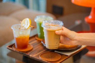 Kahve masasında elinde buzlu latte tutan biri. Yanında da espresso tonik ve buzlu kibrit gibi içkiler.