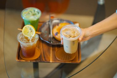 Kahve masasında elinde buzlu latte tutan biri. Yanında da espresso tonik ve buzlu kibrit gibi içkiler.