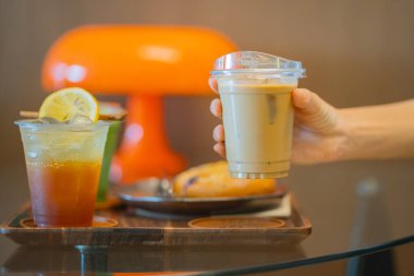 Kahve masasında elinde buzlu latte tutan biri. Yanında da espresso tonik ve buzlu kibrit gibi içkiler.