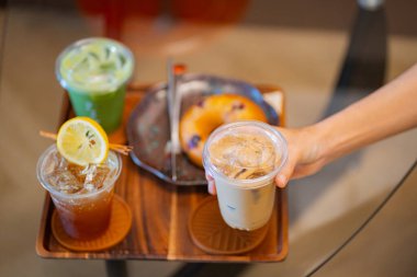 Kahve masasında elinde buzlu latte tutan biri. Yanında da espresso tonik ve buzlu kibrit gibi içkiler.