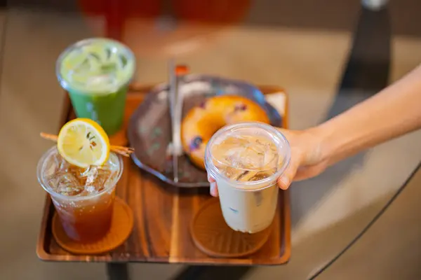 Kahve masasında elinde buzlu latte tutan biri. Yanında da espresso tonik ve buzlu kibrit gibi içkiler.