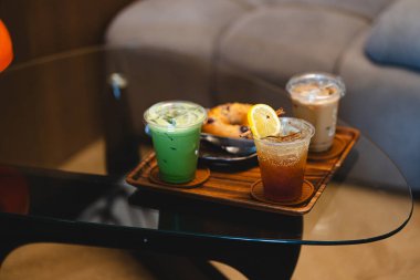 Kafedeki cam masada espresso tonik, buzlu latte ve buzlu kibrit gibi içecekler var.