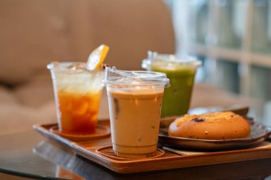 Kafedeki cam masada espresso tonik, buzlu latte ve buzlu kibrit gibi içecekler var.